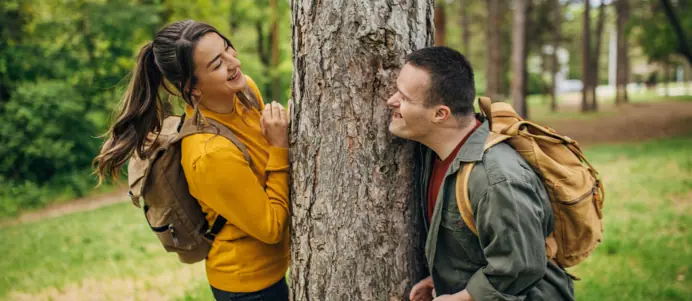 Two friends hiding behind tree and having fun while hiking